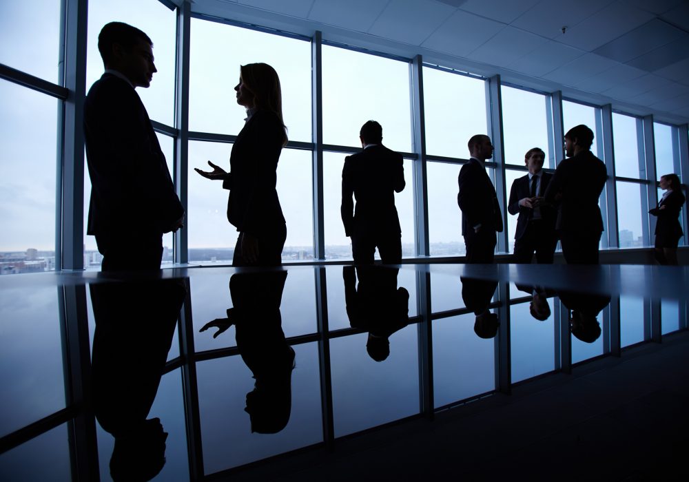 Group of colleagues standing against window in office and speaking